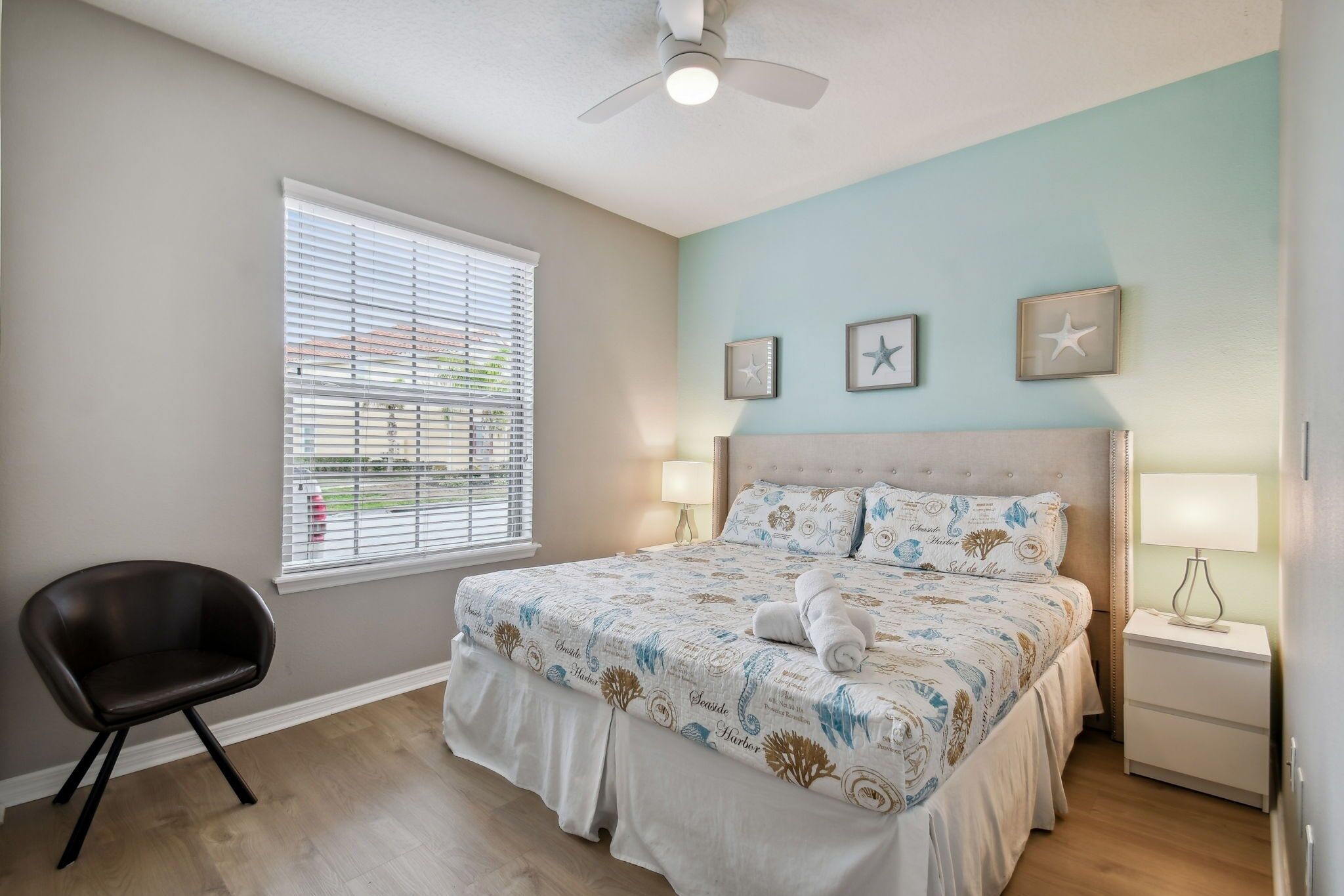 A bedroom with a bed, a chair, a nightstand, and a ceiling fan.
