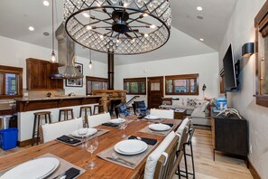 A spacious kitchen with a large dining table set for six, a chandelier, and wooden cabinets. - Town Lift Chalet by RedAwning (Park City)
