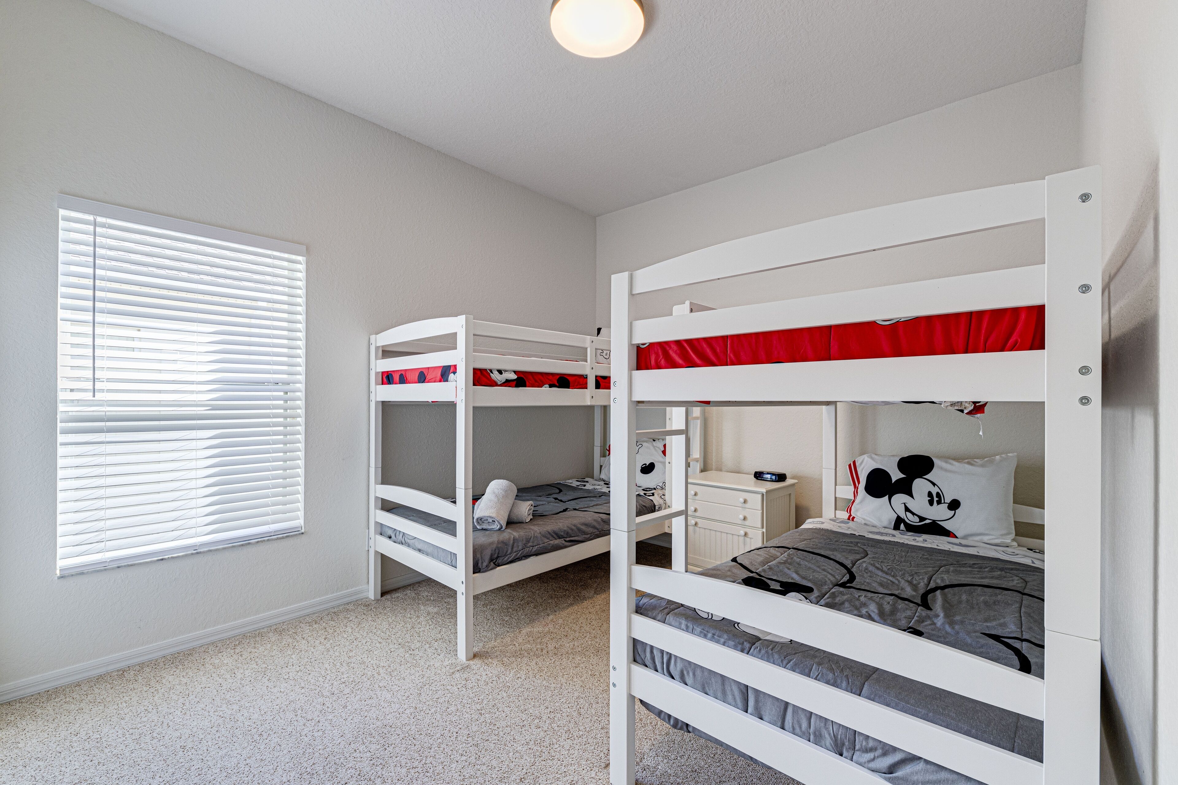 A bedroom with bunk beds, a window with blinds, and a nightstand with a lamp.