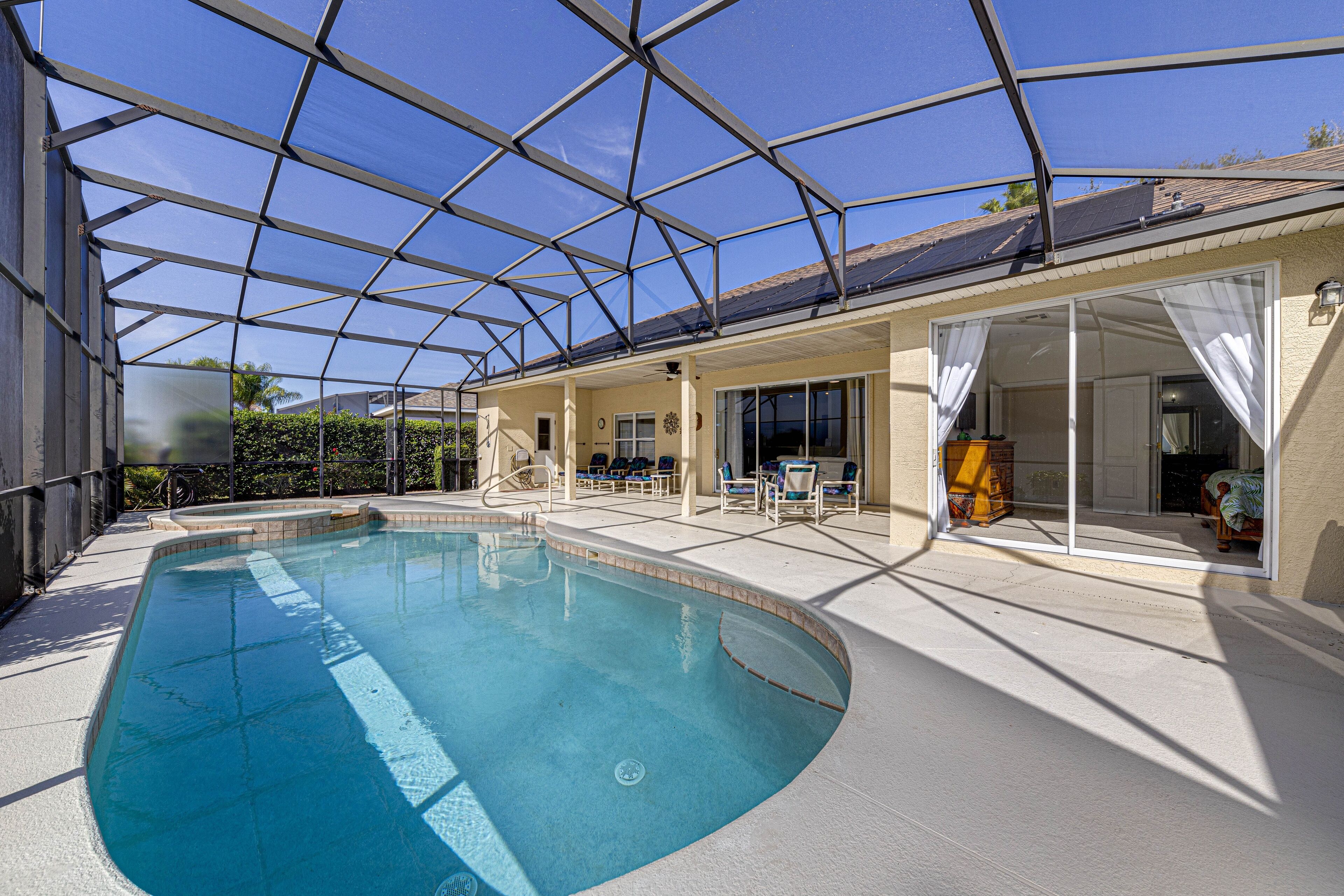 An indoor swimming pool with a glass ceiling, surrounded by lounge chairs and a covered patio area.