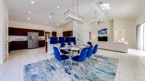 Une cuisine spacieuse avec des meubles de couleur bois foncé, un réfrigérateur en acier inoxydable et un coin repas agrémenté d’un tapis bleu et de chaises assorties.
