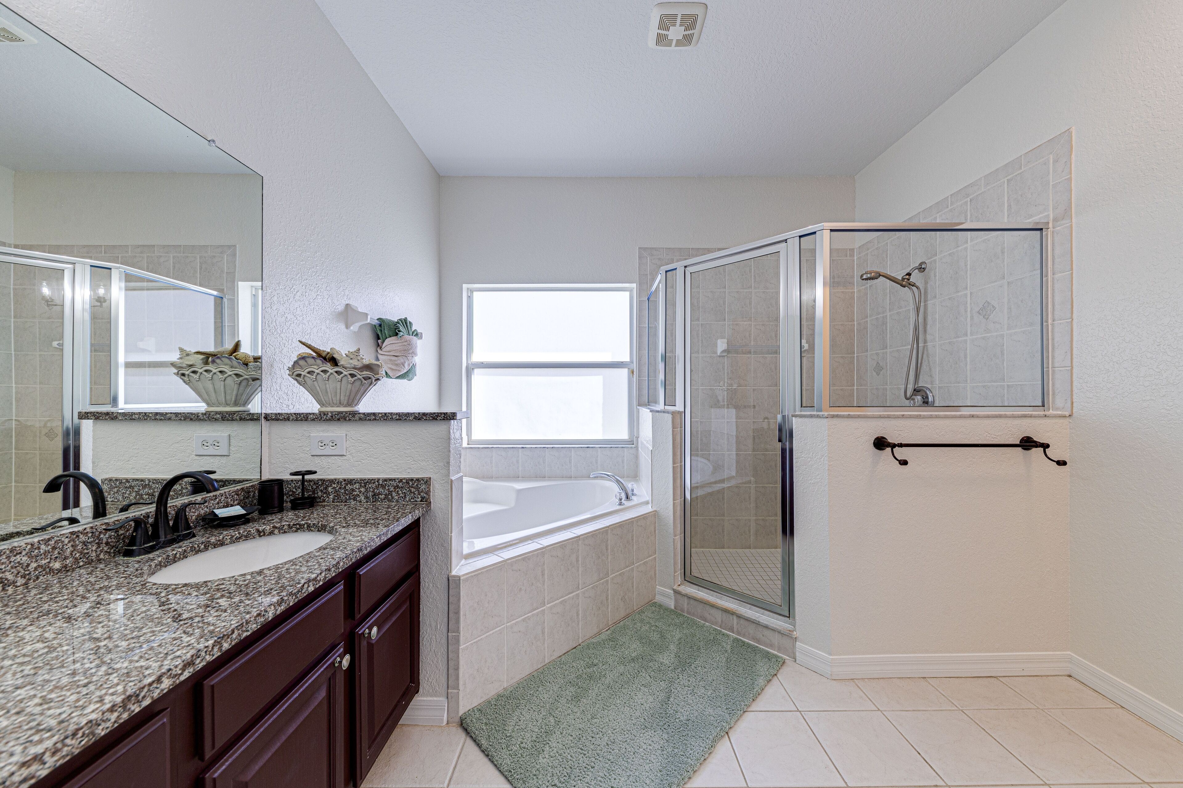 A bathroom with a double sink, a bathtub, a glass shower enclosure, and a window providing natural light.