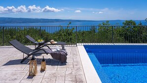 A poolside area with lounge chairs, a table with drinks, and a view of the sea. - Seaview Villa Roko with heated pool (Jesenice, Dugi Rat)