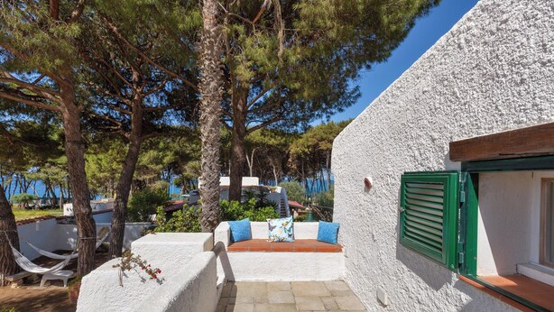 A white-walled building with a green shuttered window, a stone-paved patio, and a hammock.