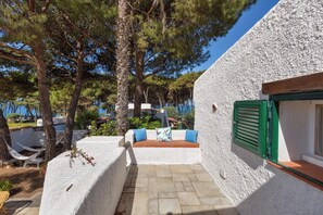 Un edificio dalle pareti bianche con una finestra con persiane verdi, un patio in pietra e un'amaca.