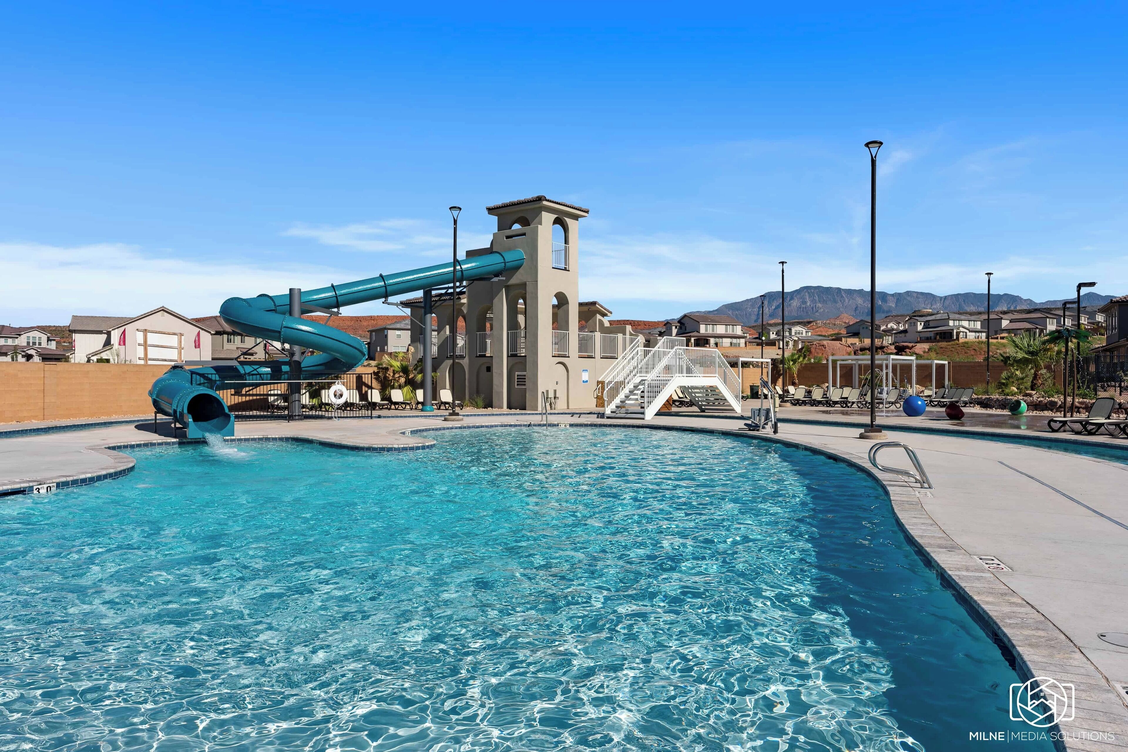 A swimming pool with a water slide, a tower structure, and a view of houses in the background.