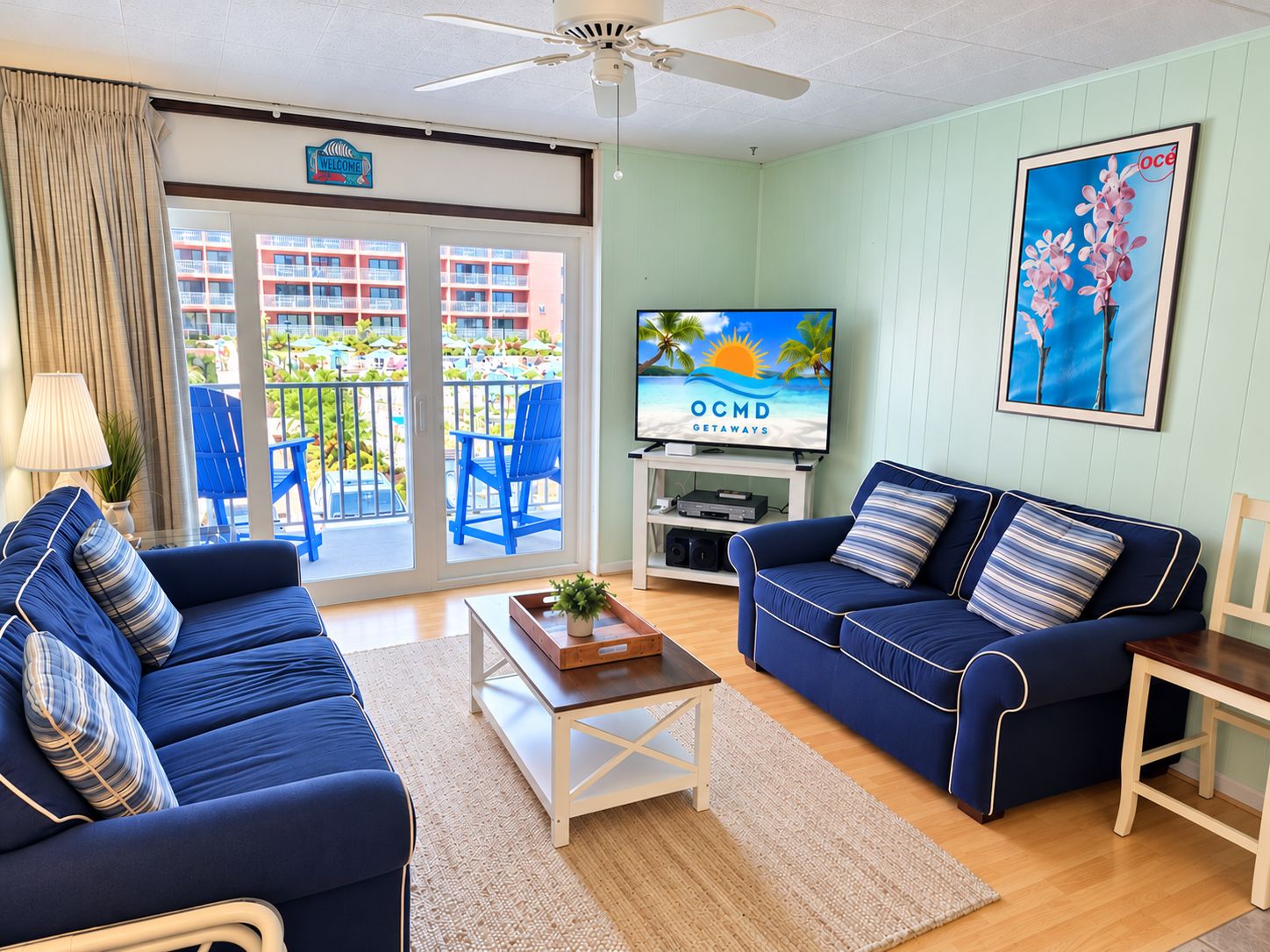 A living room with two blue sofas, a coffee table, a TV, and a balcony with chairs and a view of buildings.