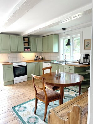 A kitchen with green cabinets, a wooden dining table, and a coffee machine.