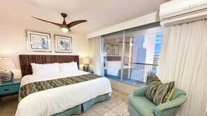 Een hotelkamer met een bed, een plafondventilator, een balkon met gordijnen en een airconditioning.