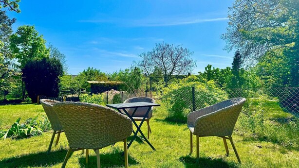 Zona relax all'aperto con sedie in vimini e un tavolo, circondata da vegetazione lussureggiante e alberi.