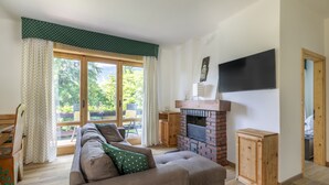 Un salon avec un canapé, une cheminée, un téléviseur et une vue sur la verdure à l’extérieur.