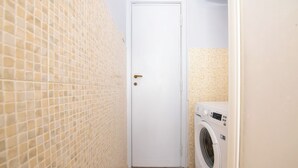 Ein Waschraum mit weißer Tür, einer Waschmaschine und Fliesenwänden.