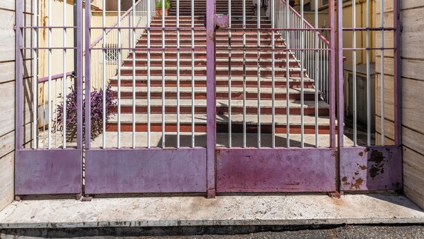 Ein verschlossenes Eingangstor mit einer Treppe, die zu einem Gebäude mit Balkonen führt.