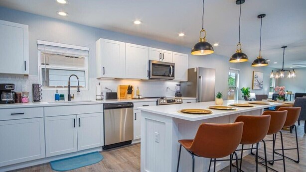 A modern kitchen with white cabinets, stainless steel appliances, and a central island with bar stools. - Spacious Delightful 4 BR/ 3 BA Close to Downtown (San Antonio)