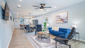 A modern living room with a blue sofa, a coffee table, and a black chair. There is a dining area with a table and chairs in the background. - Spacious Delightful 4 BR/ 3 BA Close to Downtown (San Antonio)