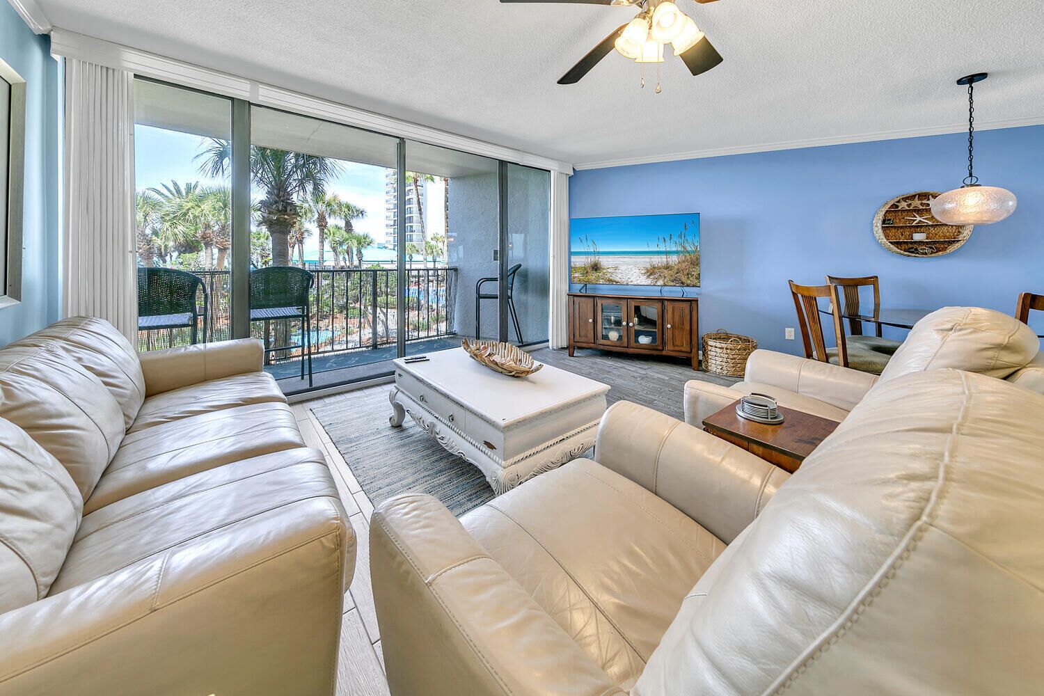 A spacious living room with a beige leather sofa, a white coffee table, and a dining area with a wooden cabinet and chairs.
