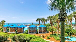 A resort with multiple blue-roofed cabanas, a pool, and palm trees. - ⛵Stunning Gulf Front-Lagoon Pool-Edgewater 1-105⛵ (Panama City Beach)