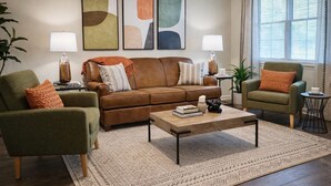 A living room with a brown leather sofa, two armchairs, a coffee table, and a patterned rug. There are abstract paintings on the wall, two lamps, and a window with curtains. - 5 Minutes to VSU, I-75 & Restaurants! Sleeps 5 w/ 2 Full Baths- Family Friendly (Remerton)