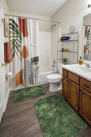 A bathroom with a shower curtain featuring leaf patterns, a toilet, a sink with a mirror, and wooden cabinets.