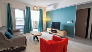 A modern living room with a sofa, a red chair, a wooden coffee table, a TV on a wooden stand, and a floor lamp. - EVASION SAINT LEU, APARTMENT 100 M FROM THE SEA  (Saint-Leu)