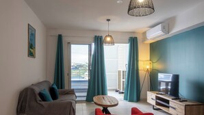 A living room with a sofa, a red chair, a wooden TV stand, and a view through the glass door. - EVASION SAINT LEU, APARTMENT 100 M FROM THE SEA  (Saint-Leu)