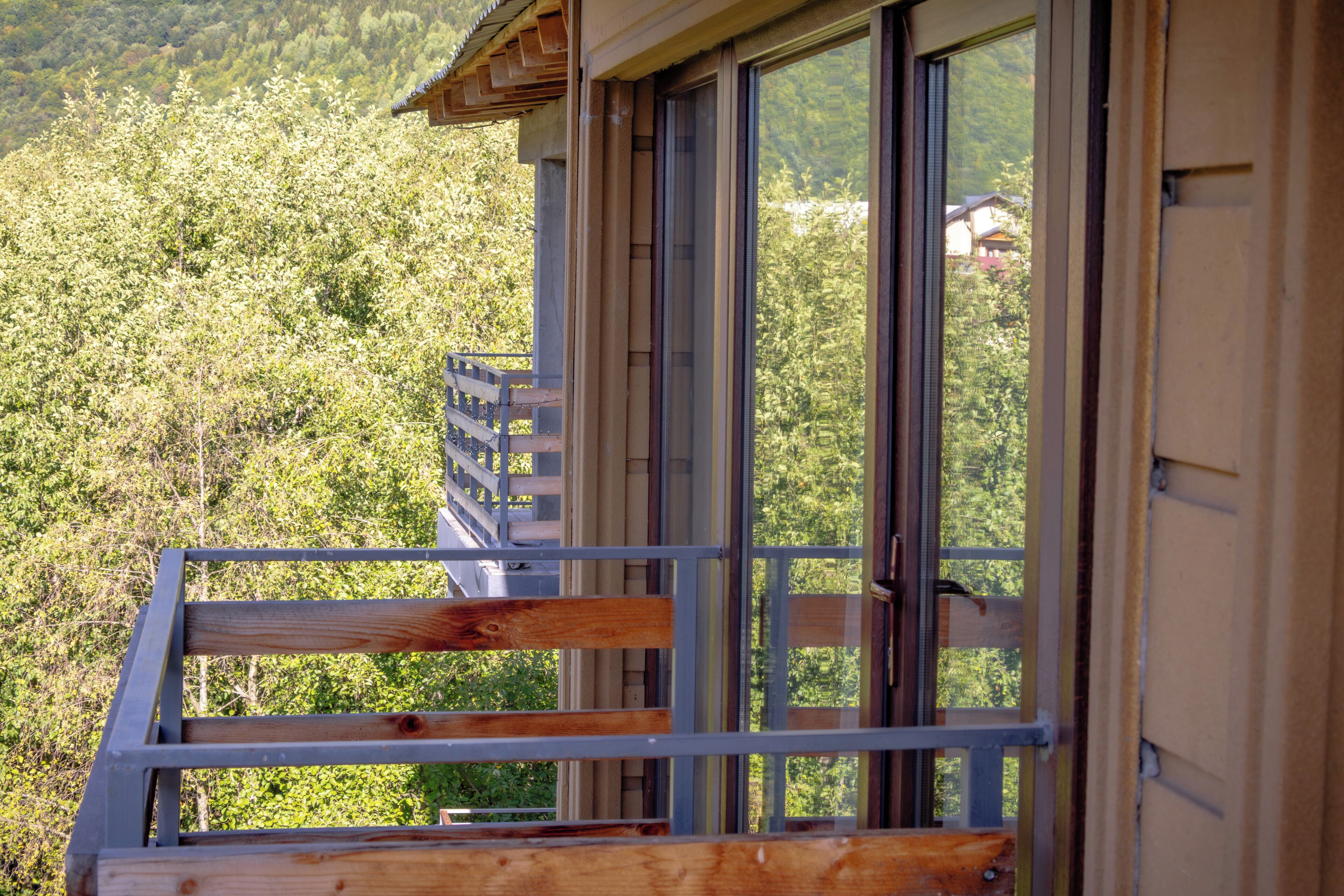 Un balcon en bois, doté de rampes en métal, qui offre une vue sur une colline boisée.