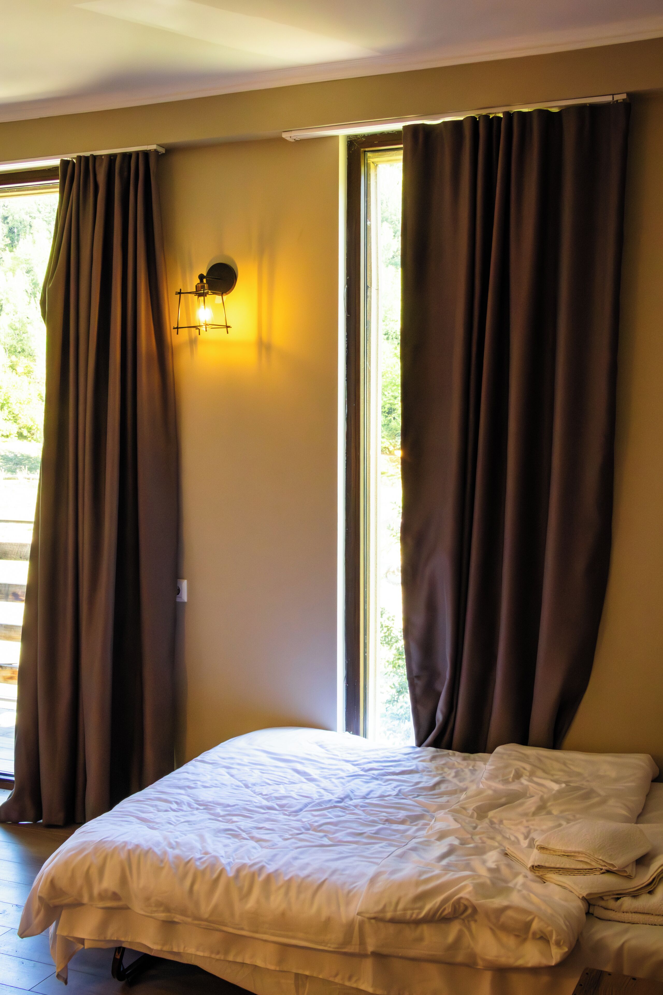 A room with a bed, curtains, a wall-mounted light, and a window.