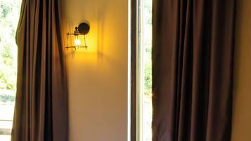 A room with a bed, curtains, a wall-mounted light, and a window.