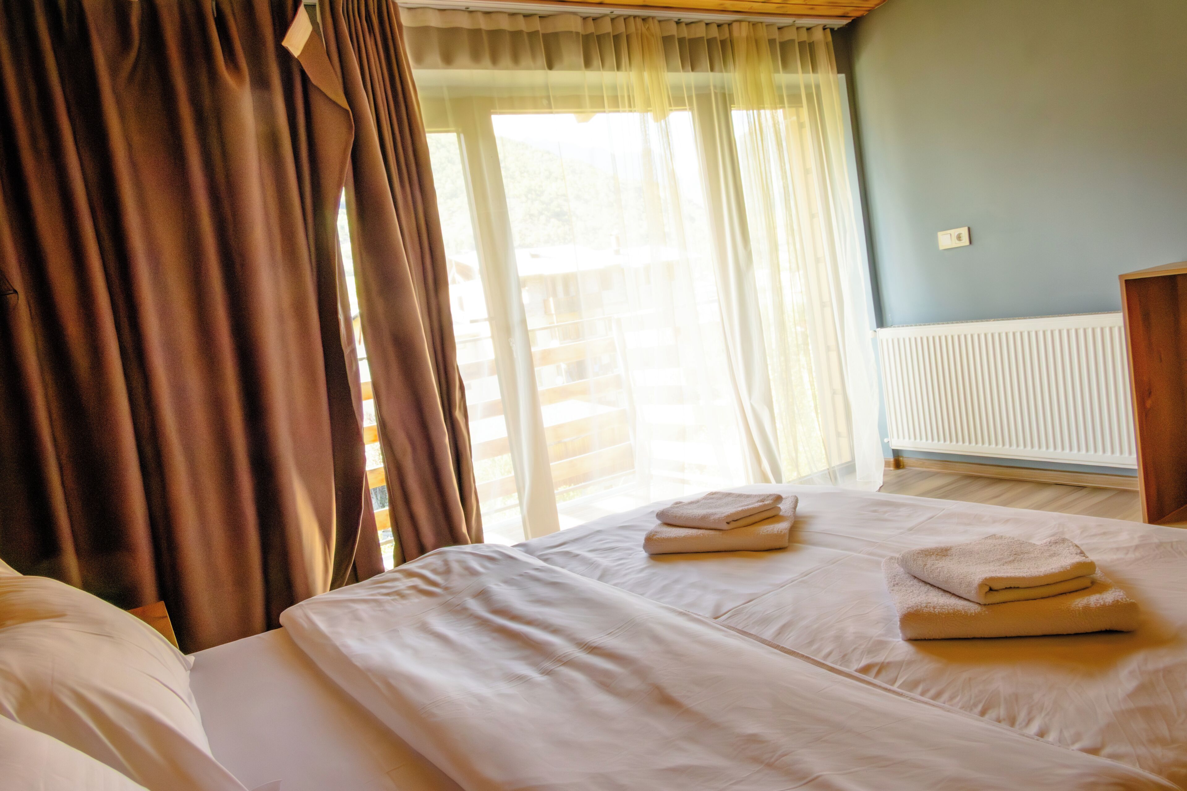A hotel room with a bed, a window with curtains, and a radiator.