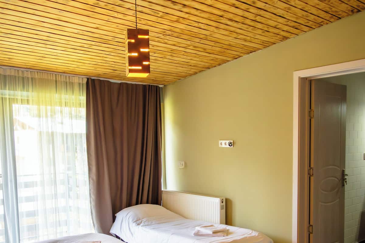 A bedroom with a wooden ceiling, two beds, a radiator, and a door leading to another room.