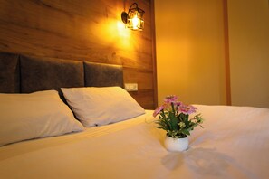 Una cama con ropa de cama blanca, cabecera de madera y un jarrón blanco con flores sobre la cama.