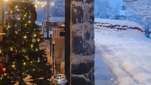 A snow-covered exterior with a stone pillar, a Christmas tree, and a metal heater.
