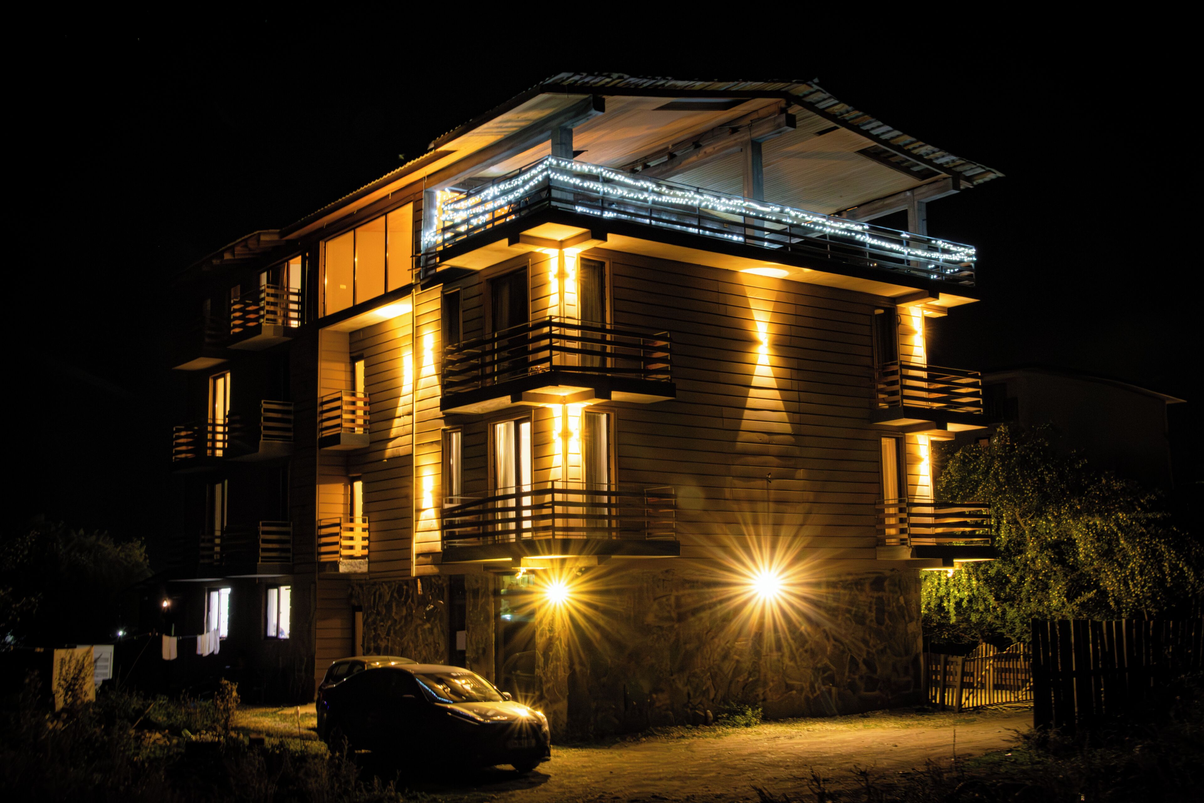 Un immeuble à plusieurs étages doté de balcons, une voiture garée devant, et une façade bien éclairée la nuit.