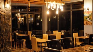 A restaurant interior with stone walls, wooden ceiling beams, and hanging light fixtures. Tables and chairs are arranged for dining.