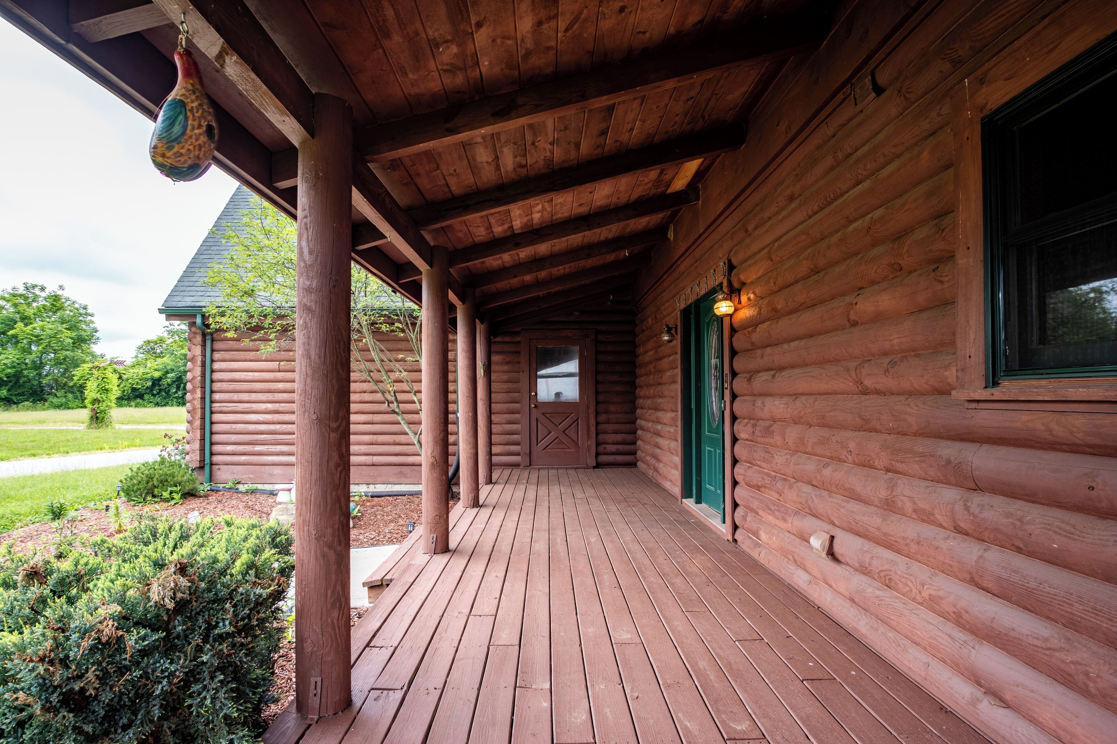 Una cabaña de madera con porche cubierto, puerta verde y una ventana.