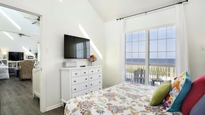 A bedroom with a bed, a TV, a dresser, and a window with a view of the ocean.