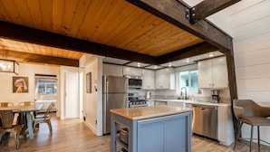 A modern kitchen with a central island, stainless steel appliances, and a wooden ceiling.