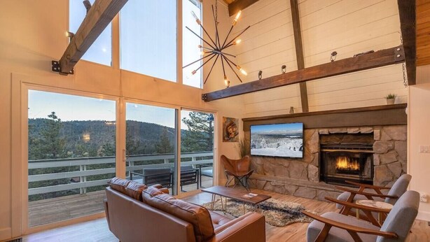 A spacious living room with a stone fireplace, large windows, and a view of the outdoors.