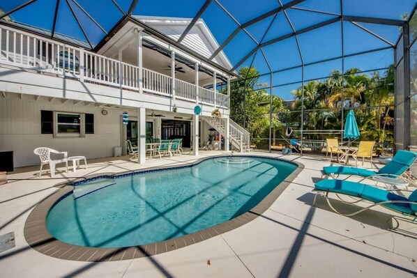 A pool area with a clear blue pool, lounge chairs, and a covered deck with a railing.
