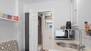 A compact bathroom with a shower, a sink with a modern faucet, a microwave, and a shelf with toiletries. - Boutique Studio Apartment By My Getaways (Brighton)