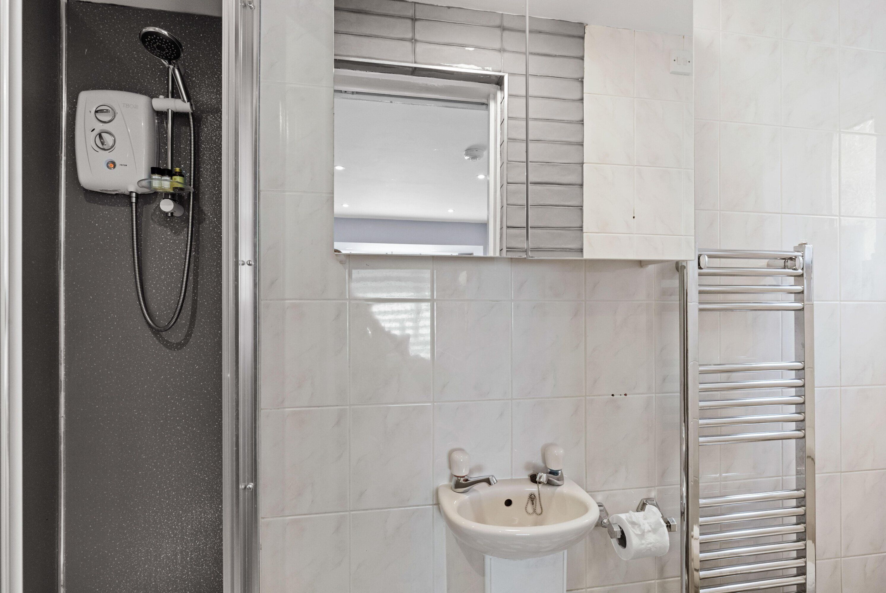 Une salle de bain avec une douche, un lavabo et un porte-serviettes.