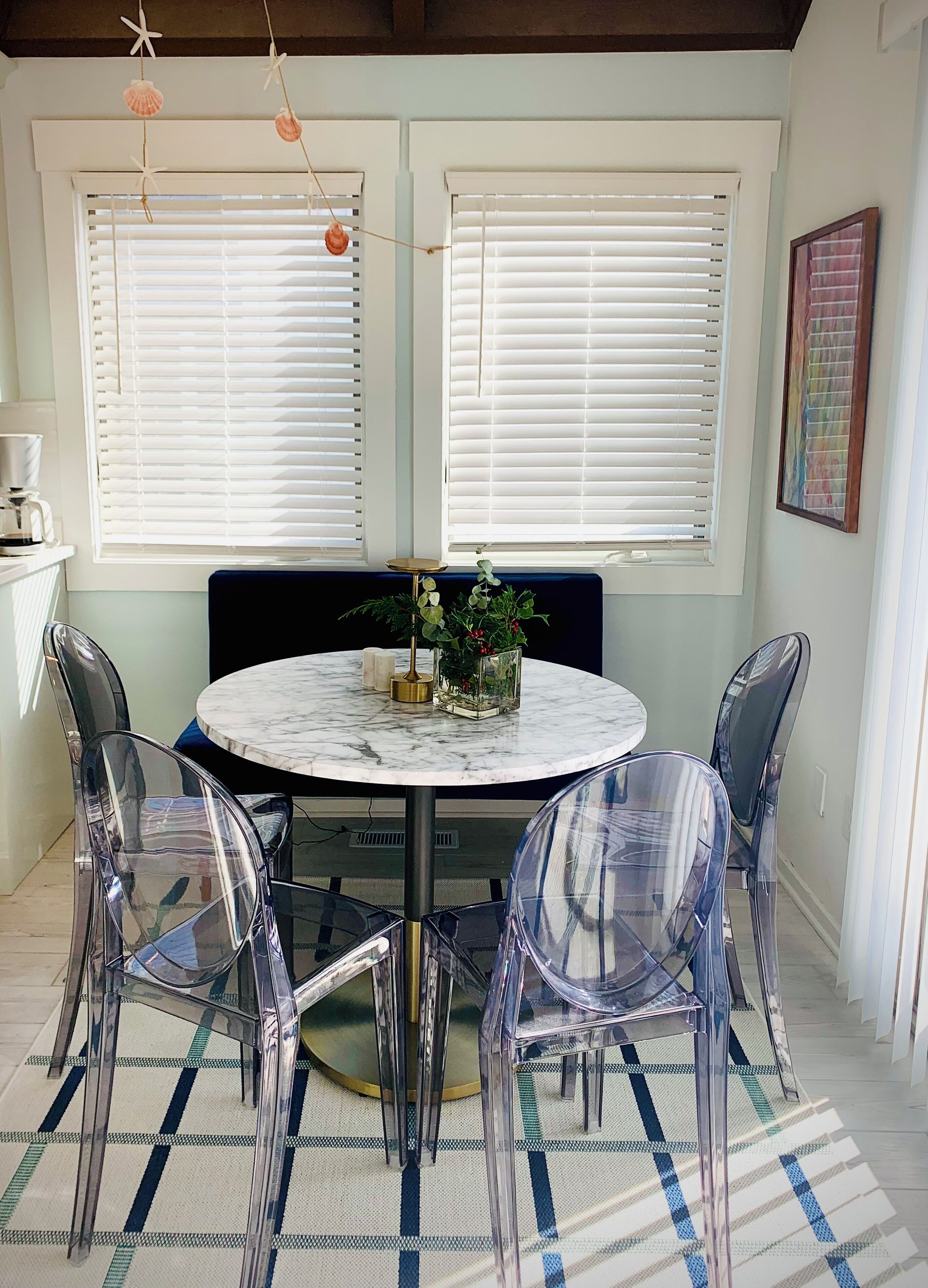 Un comedor con una mesa redonda de mármol, sillas transparentes, un sofá azul y un centro de mesa decorativo con plantas.
