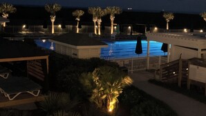 Vista notturna di una zona piscina con palme e poltrone relax.