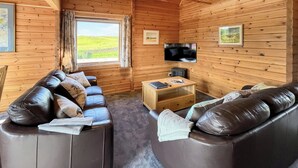 Interior acollidor d'una cabana de fusta amb sofà, televisió i finestra amb vista a un paisatge verd.