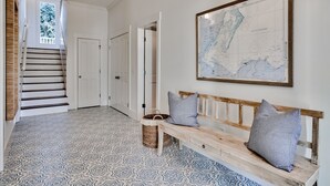 A hallway with patterned flooring, a wooden bench with pillows, a map on the wall, and a staircase with a view of greenery. - Beautiful Home in Seagrove Beach “The Chart House”, Close to Seaside and 7 minut (Santa Rosa Beach)