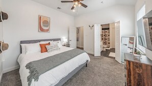 Ein Schlafzimmer mit Bett, Deckenventilator, Bad mit Duschvorhang und Spiegel.