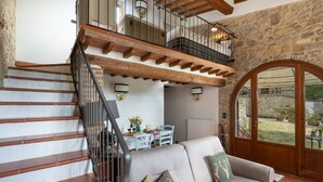 Un amplio salón con una escalera que sube a un nivel superior, un sofá acogedor y vistas al exterior a través de un gran ventanal de arco.