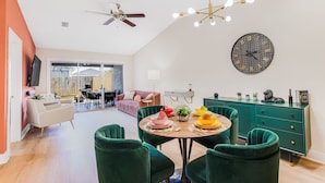 A modern dining area with a round table, green chairs, and a large wall clock.