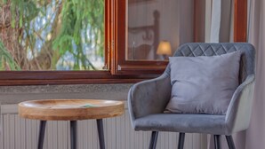A chair with a cushion and a small wooden table beside a window with a view of greenery. - Villa Bianca Lierna by Varenna Holidays (Varenna)