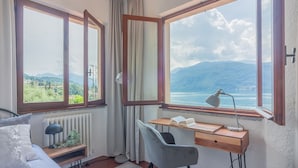 A bedroom with a bed, a desk, and a view of mountains and a body of water. - Villa Bianca Lierna by Varenna Holidays (Varenna)